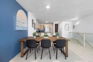 A modern dining area with a wooden table and black chairs, a kitchen in the background, and a staircase with glass railings. - Beachfront | Ocean View | Pool | Beach Access (Río Grande)