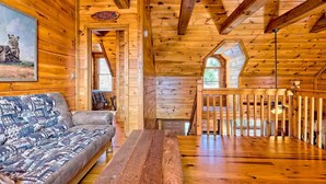 A cozy cabin interior with a wooden floor, a sofa, a dining table, and a staircase leading to an upper level.