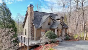 A two-story house with a stone chimney, a covered porch, and a well-maintained front yard with a small tree and mulch.