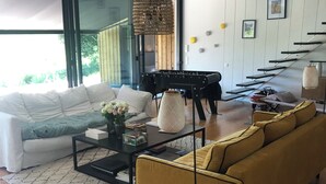Un salon moderne avec un canapé, une table basse et un divan jaune. On y trouve également un piano, un luminaire suspendu et un escalier avec une rampe.
