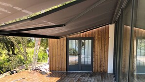 Une terrasse en bois avec une table noire et un tapis orné de motifs en forme d’étoiles.