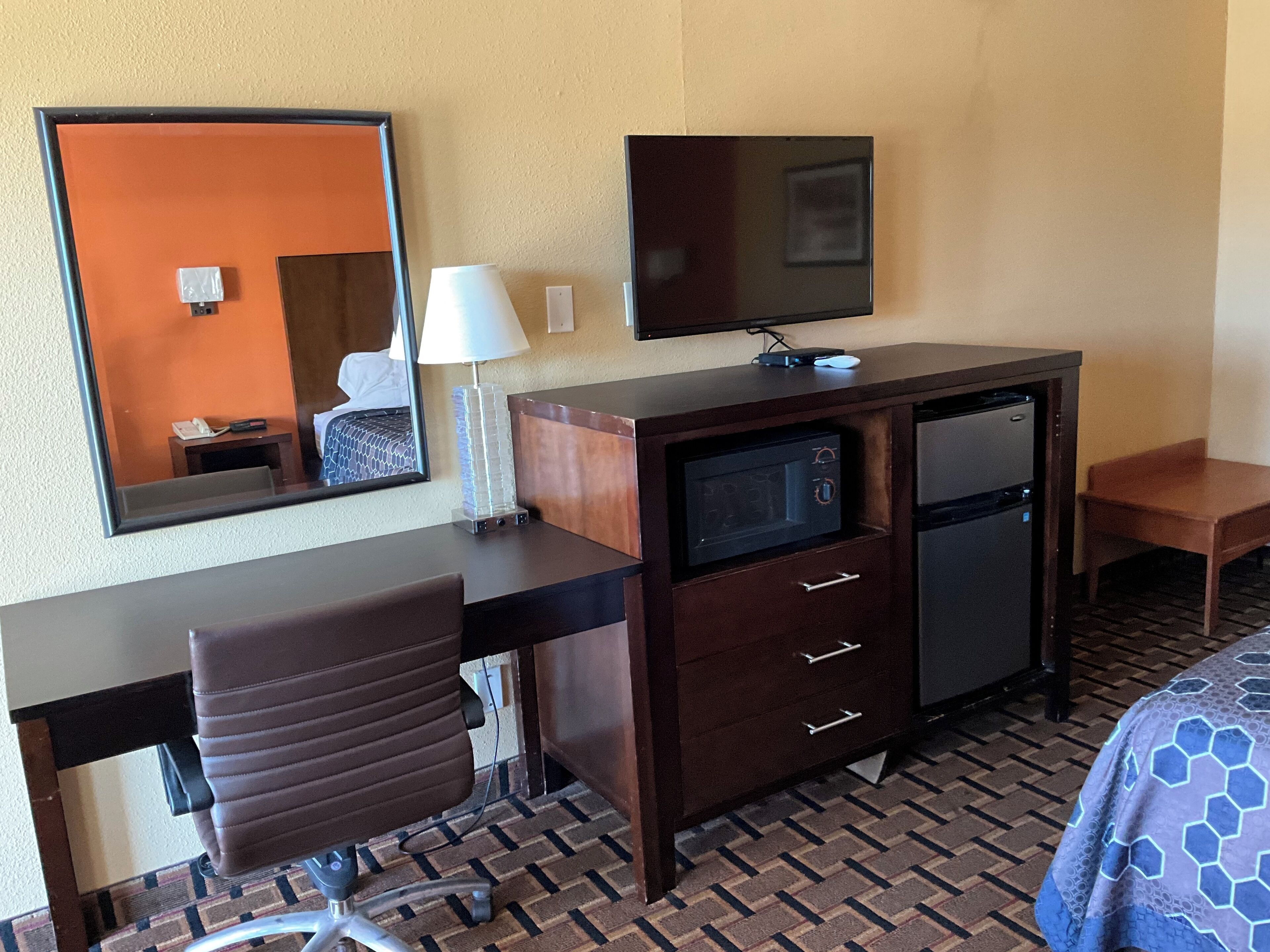 A hotel room with a wooden desk, a chair, a television, a microwave, and a refrigerator.