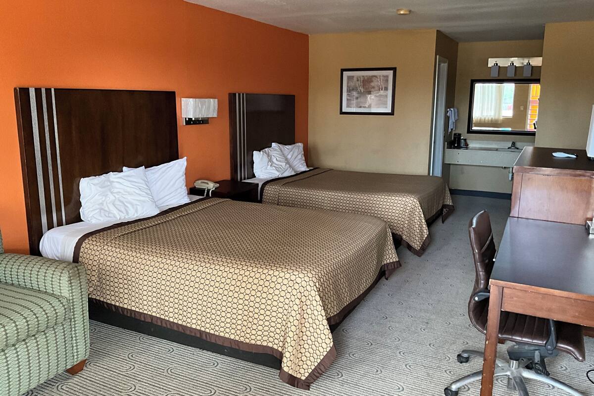 A hotel room with two beds, a desk, a chair, and a small kitchenette.