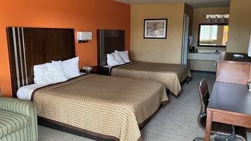 Ein Hotelzimmer mit zwei Betten, einem Schreibtisch, einem Stuhl und einer kleinen Küchenzeile.