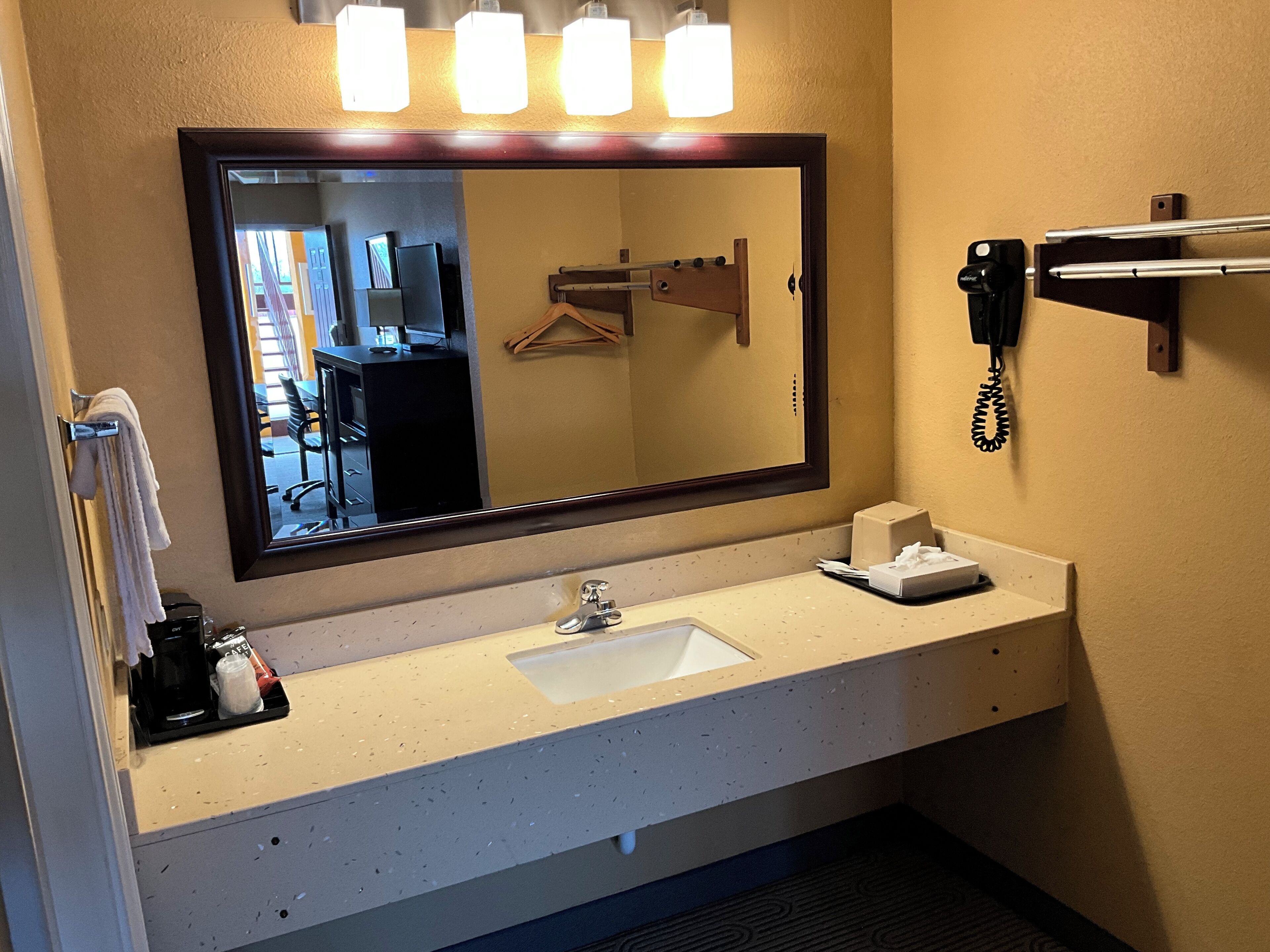 A hotel bathroom with a large mirror, a sink, a telephone, and a towel rack.