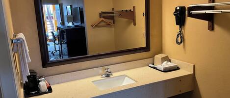 A hotel bathroom with a large mirror, a sink, a telephone, and a towel rack.