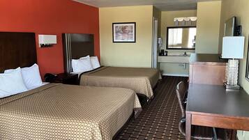 A hotel room with two beds, a desk, a chair, a sink, and a mirror.