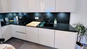 Eine moderne Küche mit weißen Schränken, einer schwarzen Arbeitsplatte, einem Spülbecken, einem Schneidebrett und einer Pflanze.