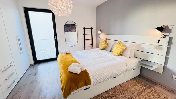 Ein modernes Schlafzimmer mit einem großen Bett, einer Nachttischlampe und Blick durch eine offene Tür.