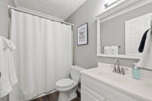 A bathroom with a white toilet, a white sink with a soap dispenser, and a shower curtain.