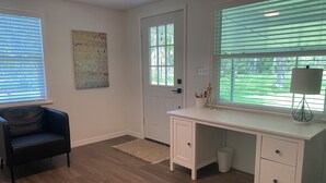 Una habitación con suelo de madera, un escritorio con cajones, una silla, una puerta y una ventana con persianas.