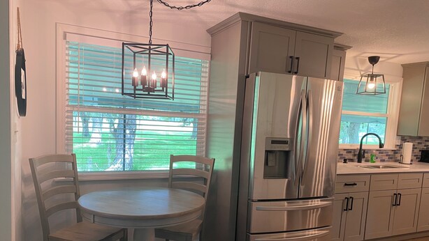 Una cocina con un refrigerador de acero inoxidable, una mesa redonda con sillas y una ventana con persianas.