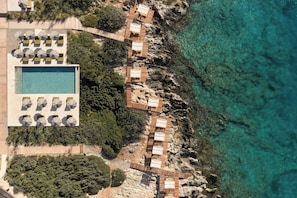An aerial view of a coastal hotel with a swimming pool, wooden deck, and beachside rooms. - JW Marriott Crete Resort & Spa (Chania)