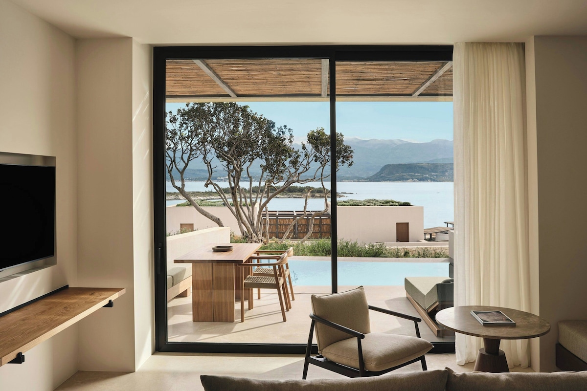 A modern room with a large sliding glass door leading to a pool and a scenic view of mountains and water.