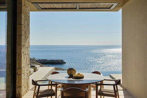A table with chairs and a bowl of fruit, overlooking a coastal view with a rocky outcrop. - JW Marriott Crete Resort & Spa (Chania)