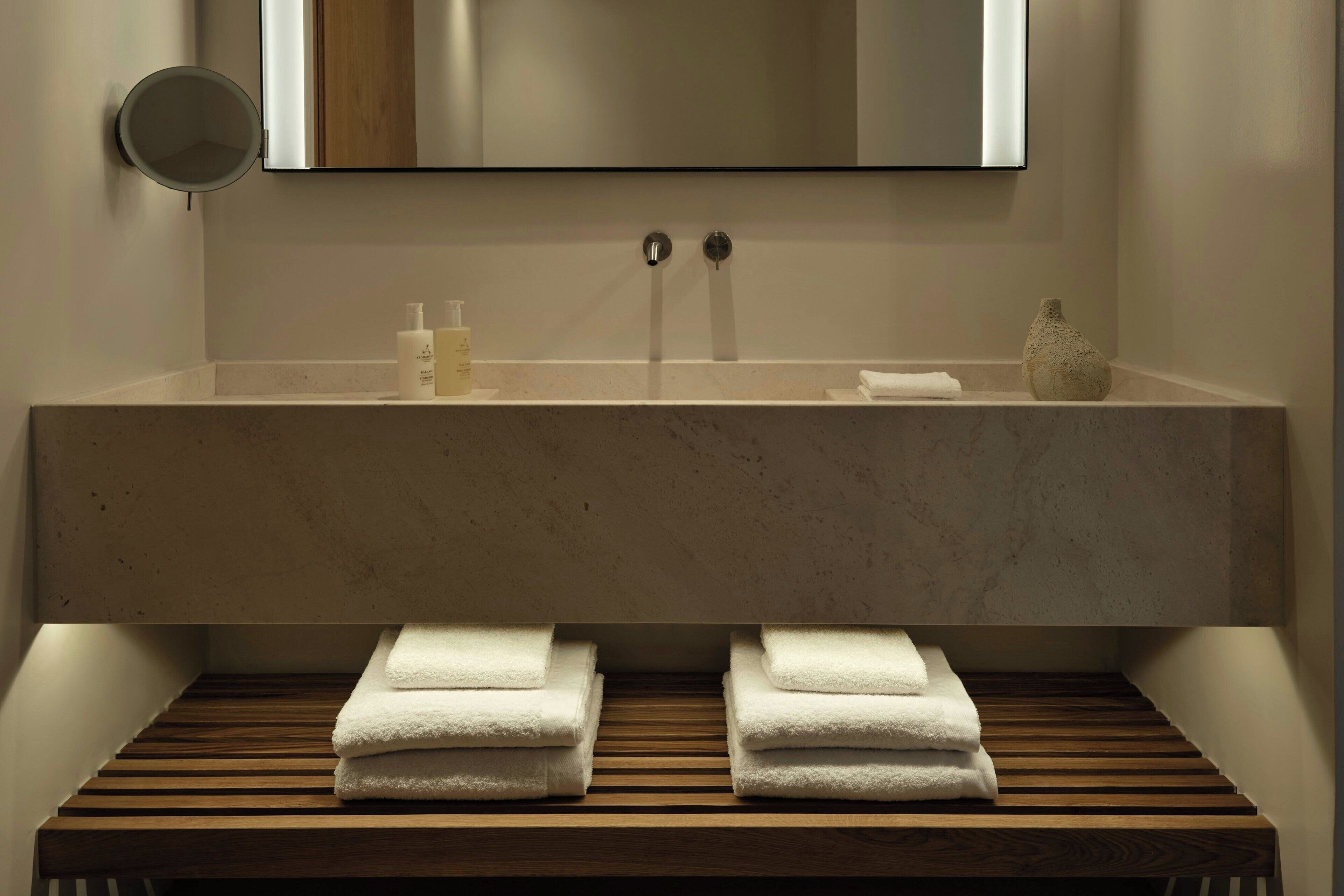 A bathroom with a large mirror, a wooden bench with towels, and a sink with toiletries.