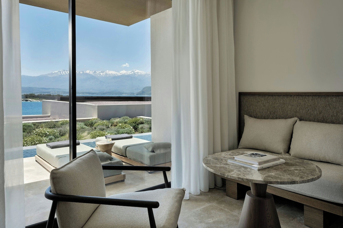 A modern room with a view of mountains, a sofa, a chair, and a round table.