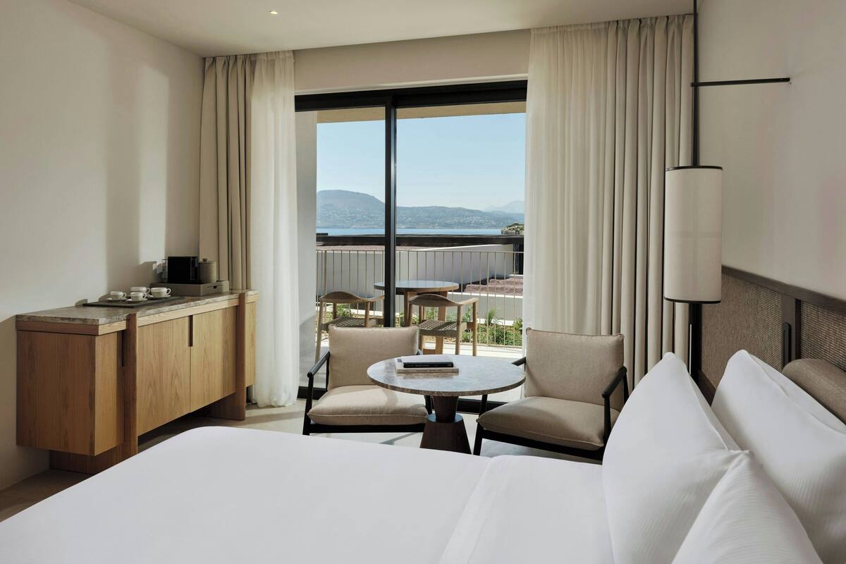 Una habitación de hotel con una cama, un escritorio, dos sillas, una mesita y vistas a la montaña.