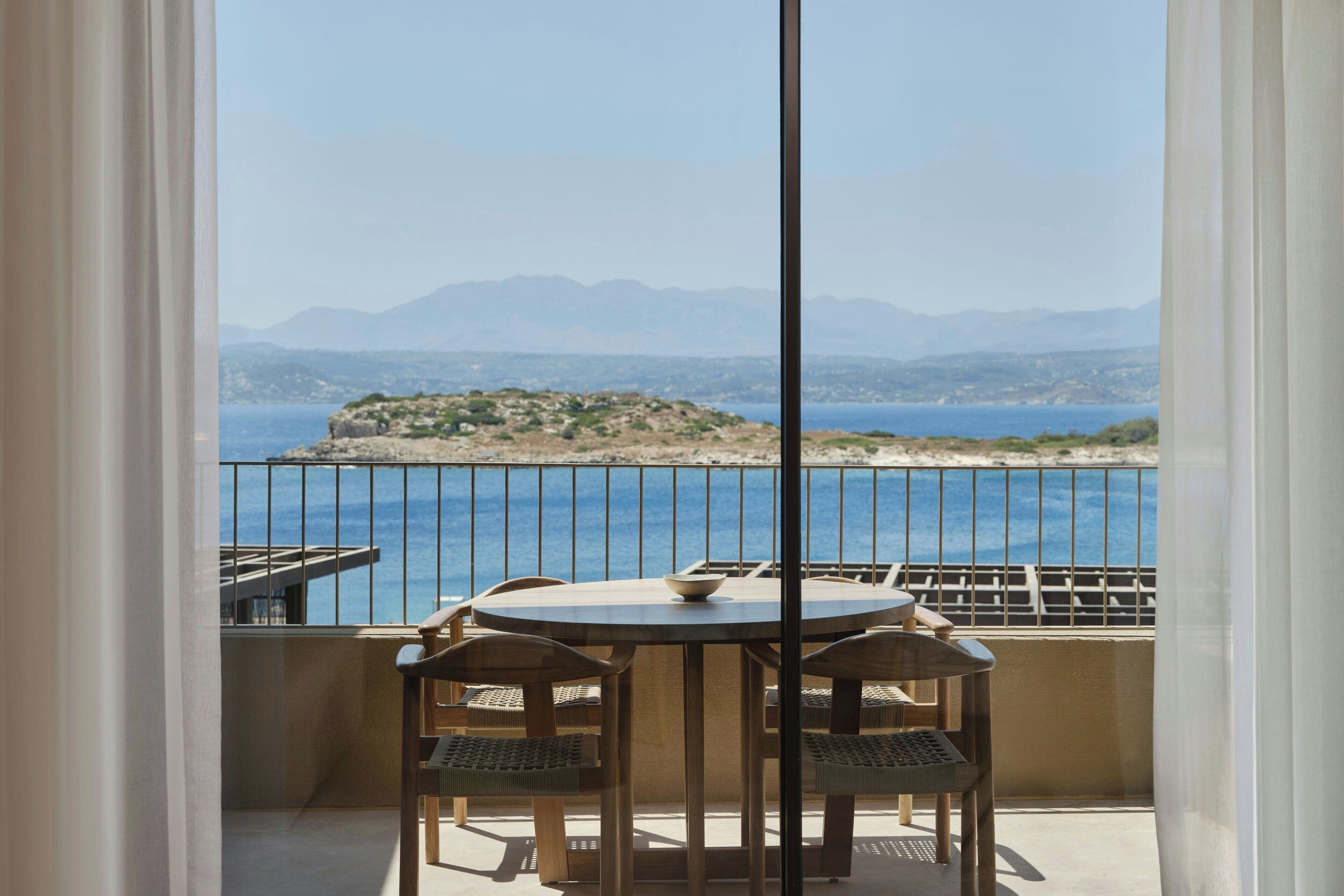 Ein Balkon mit einem runden Tisch und vier Stühlen, mit Blick auf eine Küstenlandschaft mit Bergen und einem Gewässer.