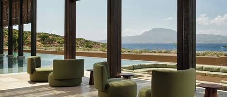 A poolside area with green cushioned seating and a view of the sea.