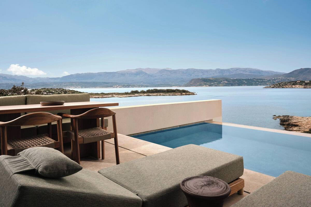 Zona junto a la piscina con vistas a montañas, una mesa, sillas y sillones de descanso.