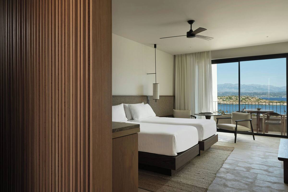 Habitación de hotel moderna con dos camas, un escritorio, una silla y vista al mar.