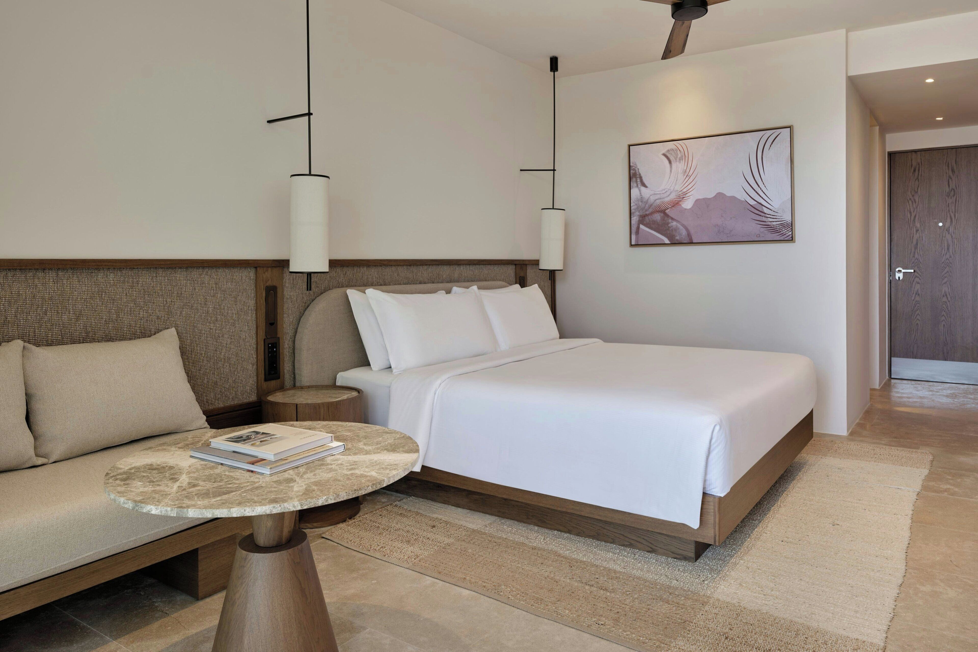 A hotel room with a bed, a sofa, a round table, and a painting on the wall.