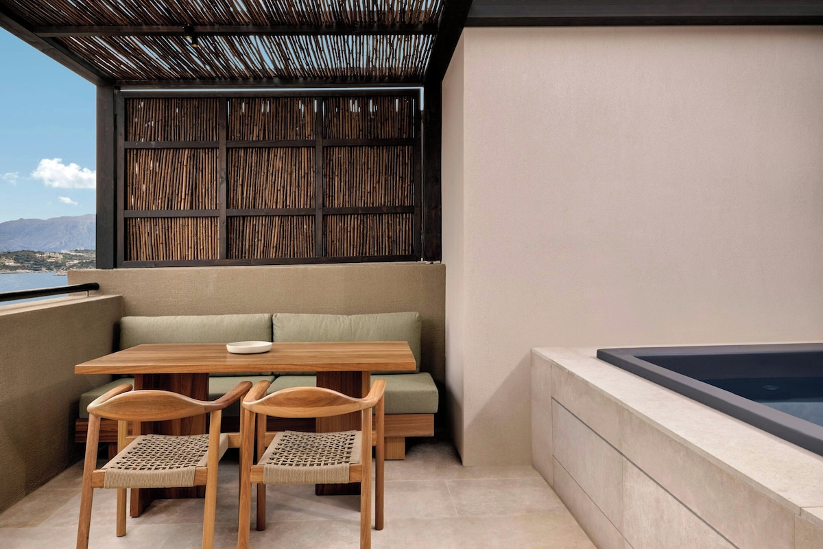 A balcony with a wooden table and chairs, a cushioned bench, and a hot tub.