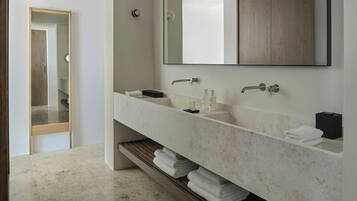 A modern bathroom with a large mirror, two sinks, and a wooden shelf with towels.