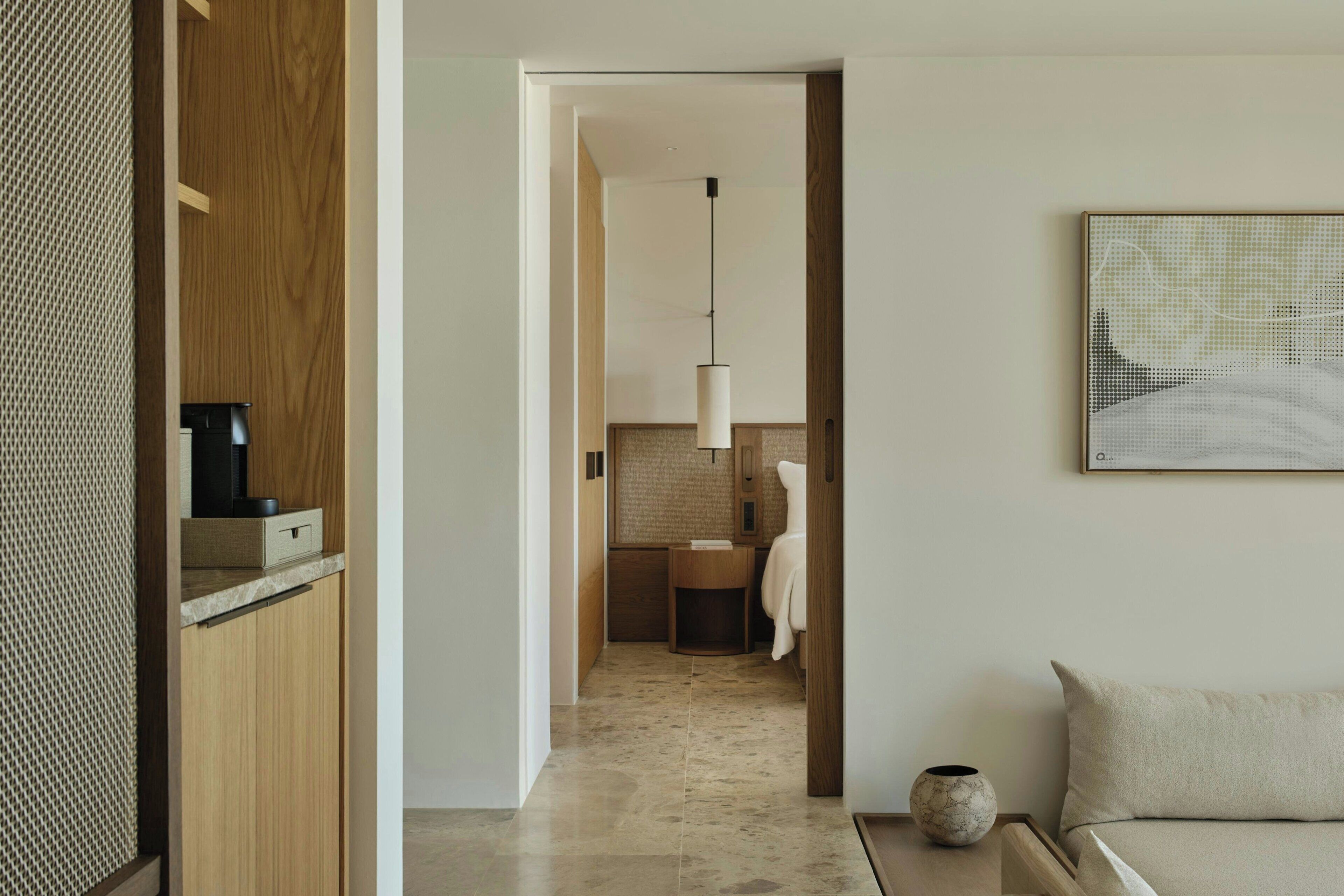 Una habitación de hotel moderna con un armario de madera, suelo de baldosas de mármol, lámpara colgante y una obra de arte enmarcada en la pared.