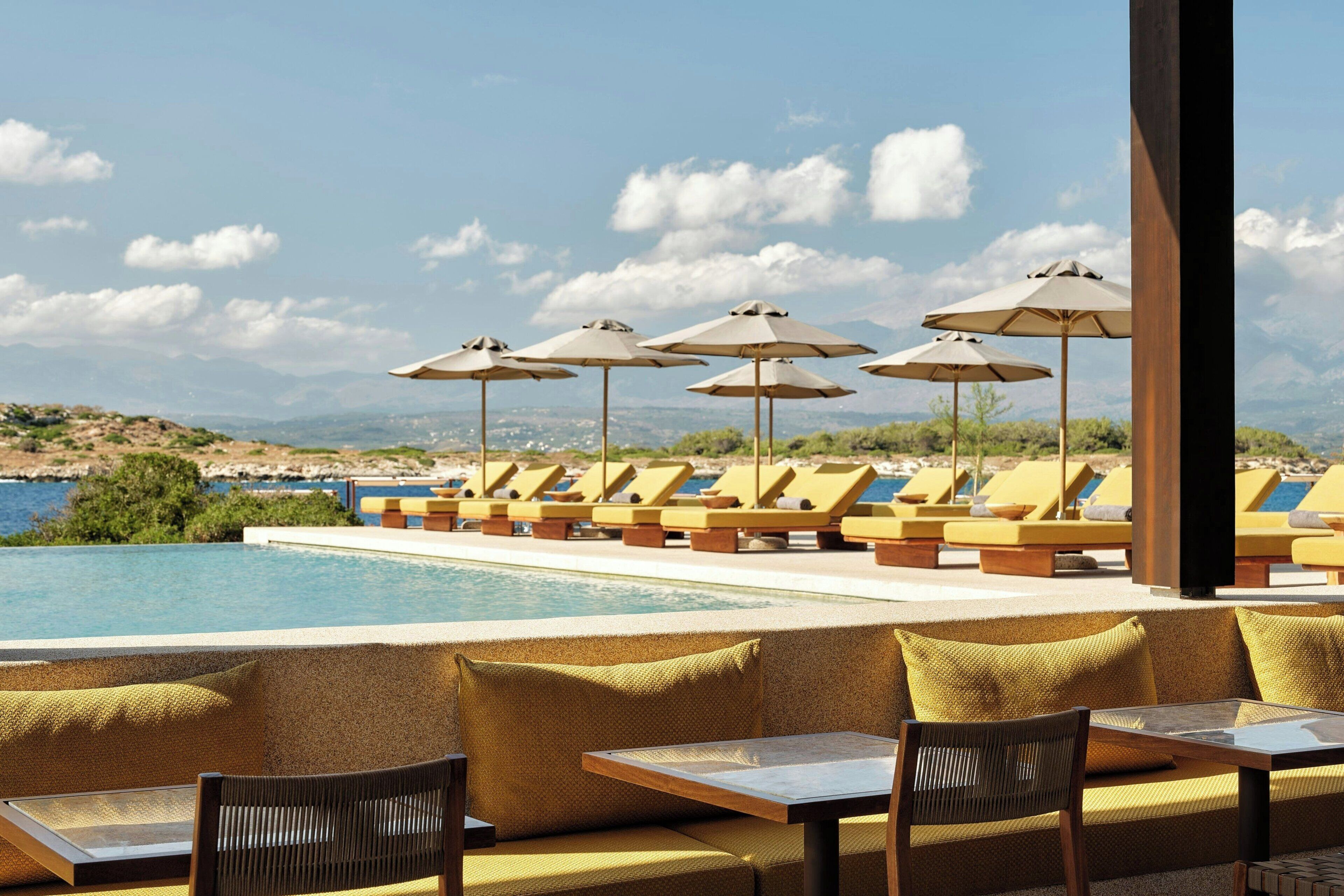 Un área junto a la piscina con sillones reclinables y sombrillas, una piscina y vistas del paisaje.