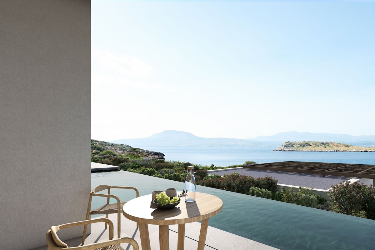 Un balcón con mesa y sillas que da a una piscina y una vista panorámica del mar y las colinas.