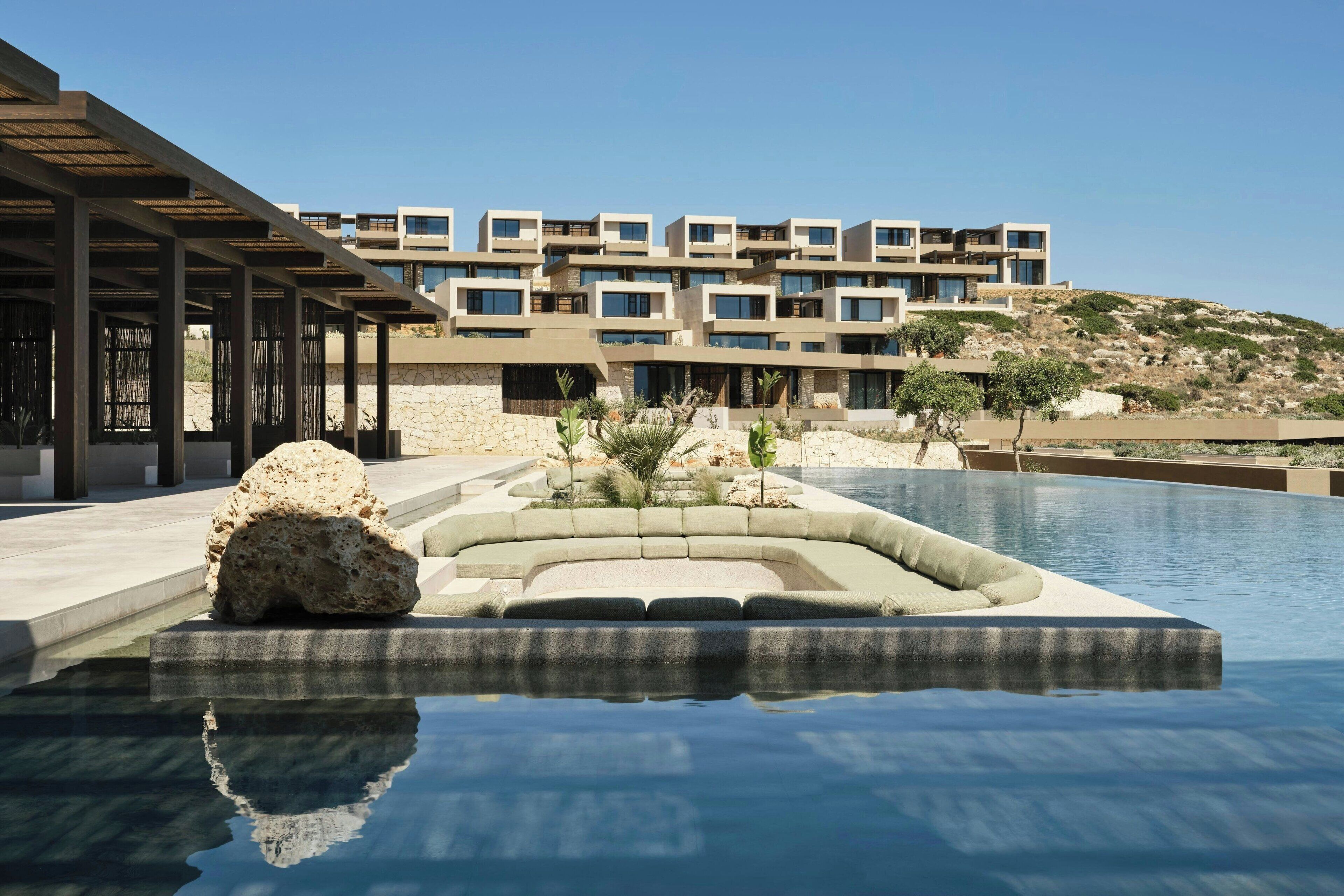 Un hotel moderno con piscina, paredes de piedra y vistas a una colina.
