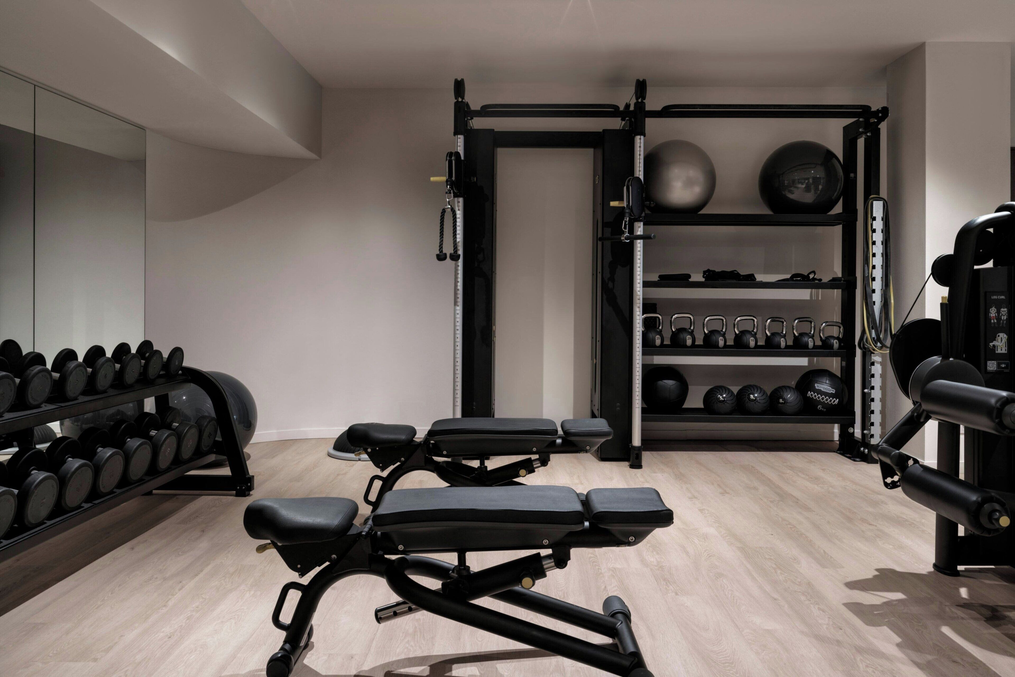 A gym with a bench press, dumbbells, kettlebells, and a squat rack.