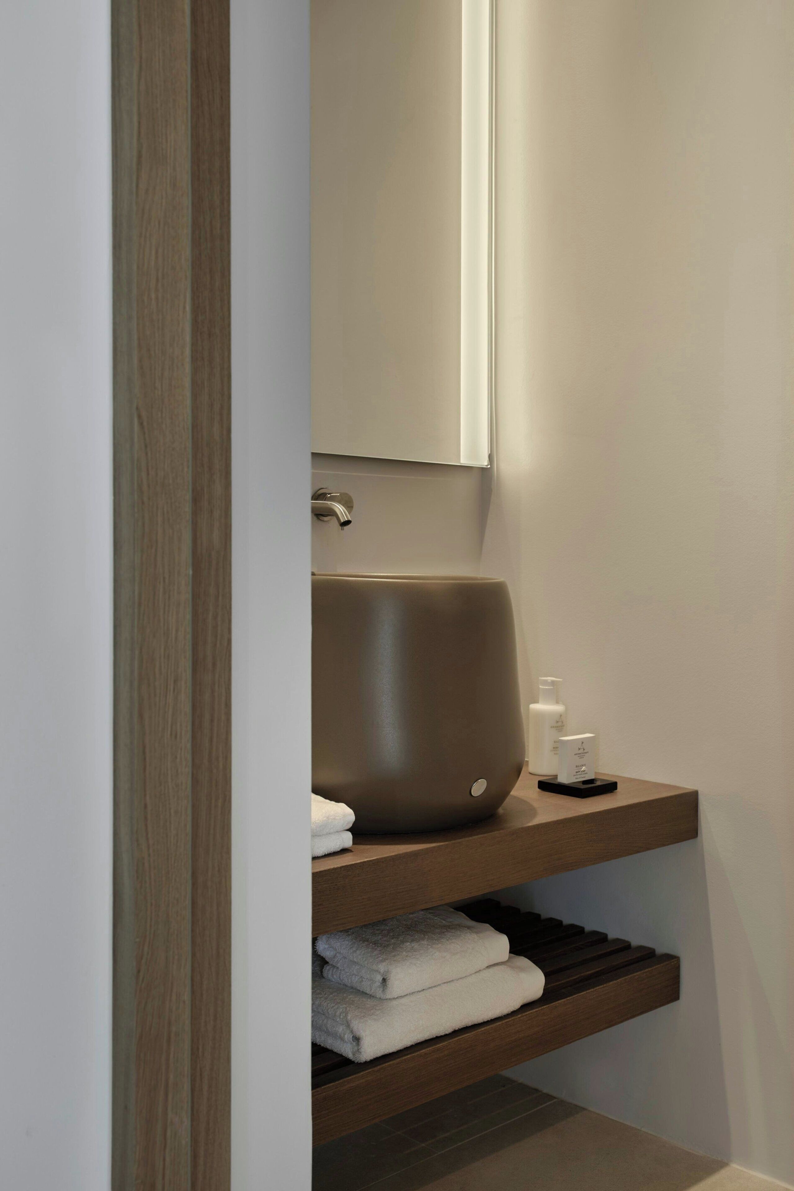 A bathroom with a large, modern sink, a mirror, and neatly folded towels on a wooden shelf.