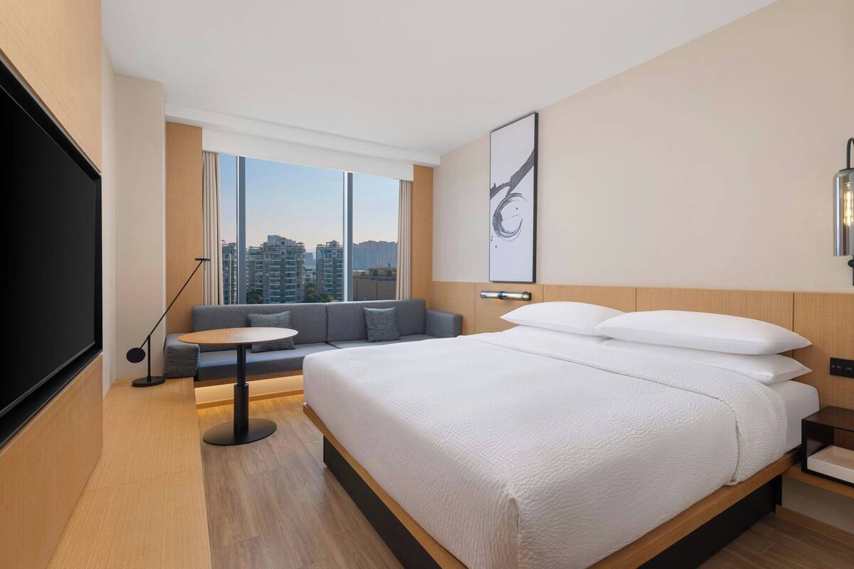 A modern hotel room with a large bed, a sofa, a small table, and a TV.
