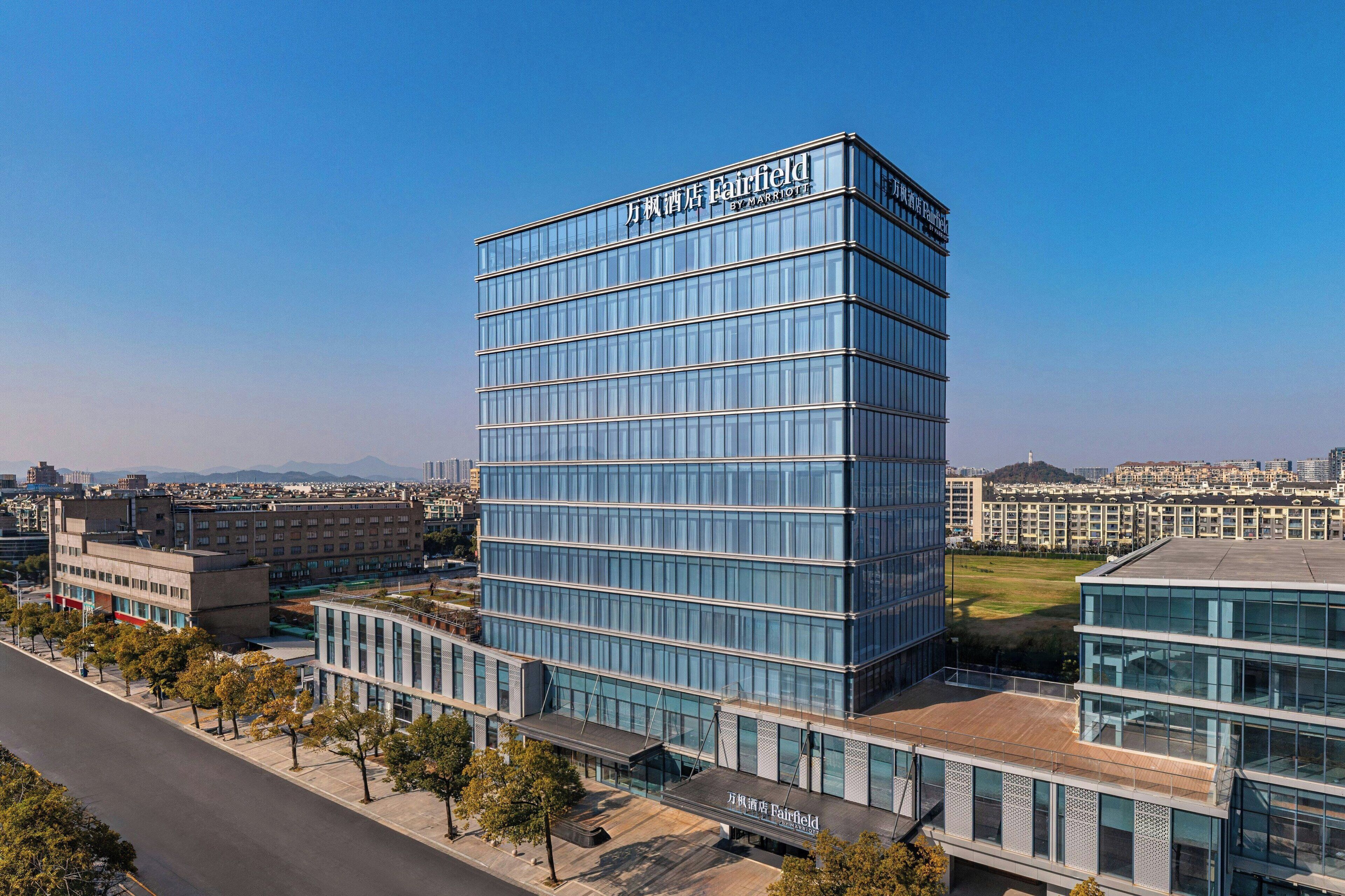 A modern hotel with a glass facade, multiple floors, and a prominent name sign.