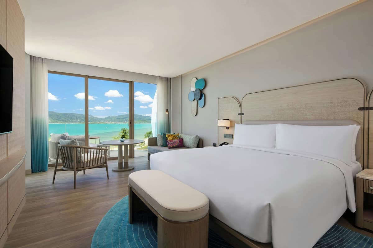 A hotel room with a large bed, a desk, a chair, and a view of the ocean.