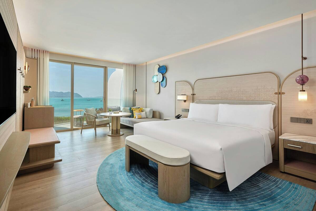 A modern hotel room with a large bed, a desk, and a seating area with a view of the sea.