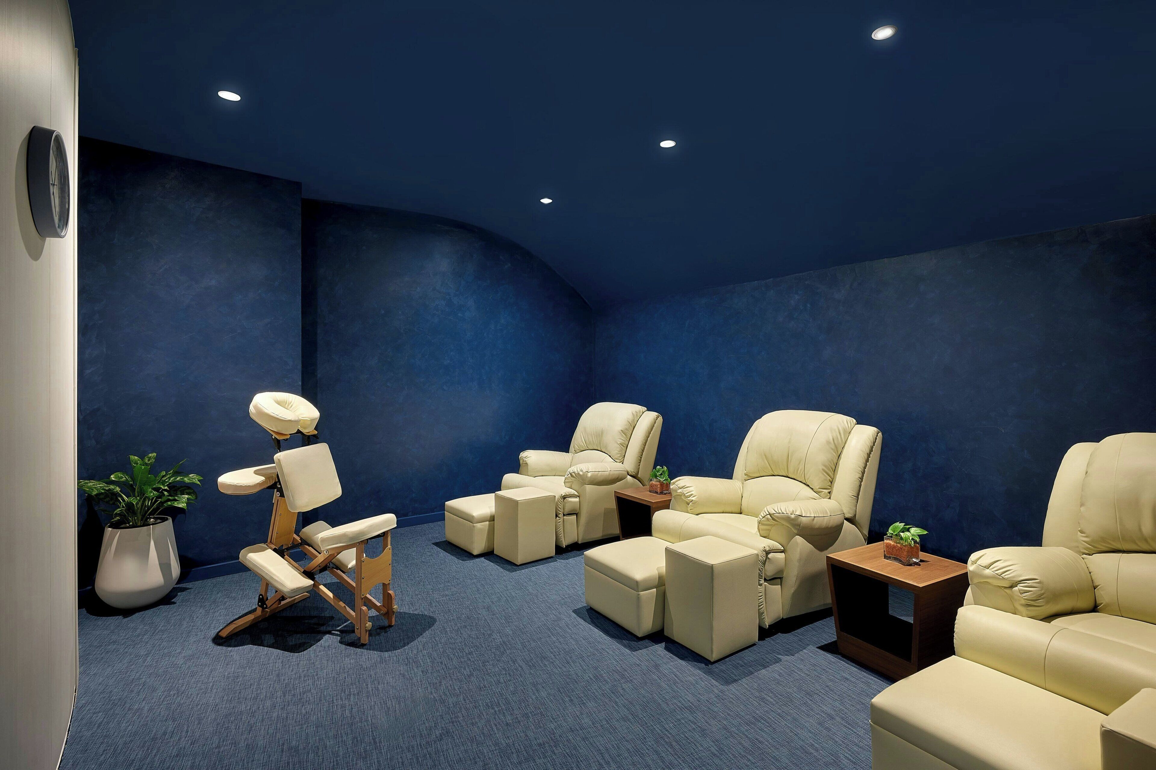 A massage therapy room with reclining chairs, a massage table, and potted plants.