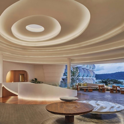 A modern interior with a central seating area, a reception desk, and a view of the sea.