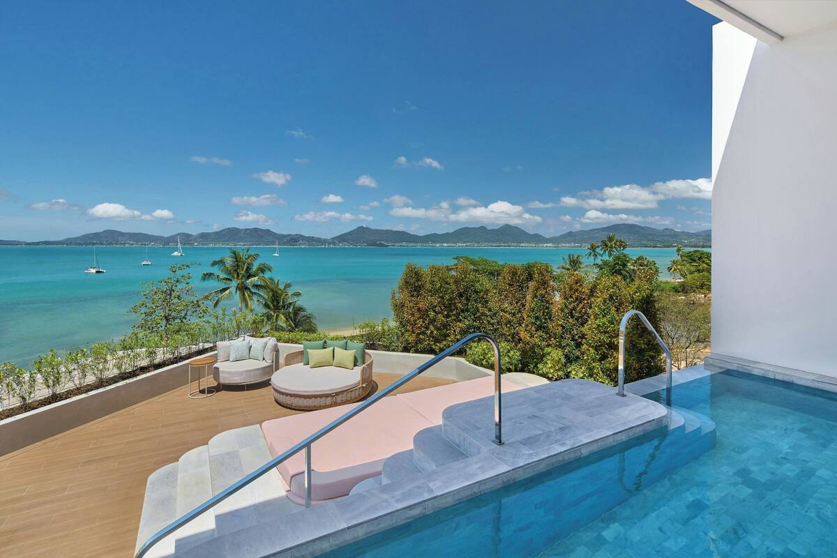 A pool area with a view of the ocean and mountains, a seating area with cushions, and a staircase leading to the pool.