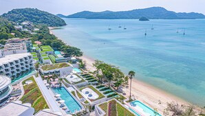 Un resort con varias piscinas, una playa y vistas al mar con barcos.