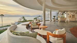 Un espacio lounge moderno al aire libre con asientos, vistas al mar y una estantería.
