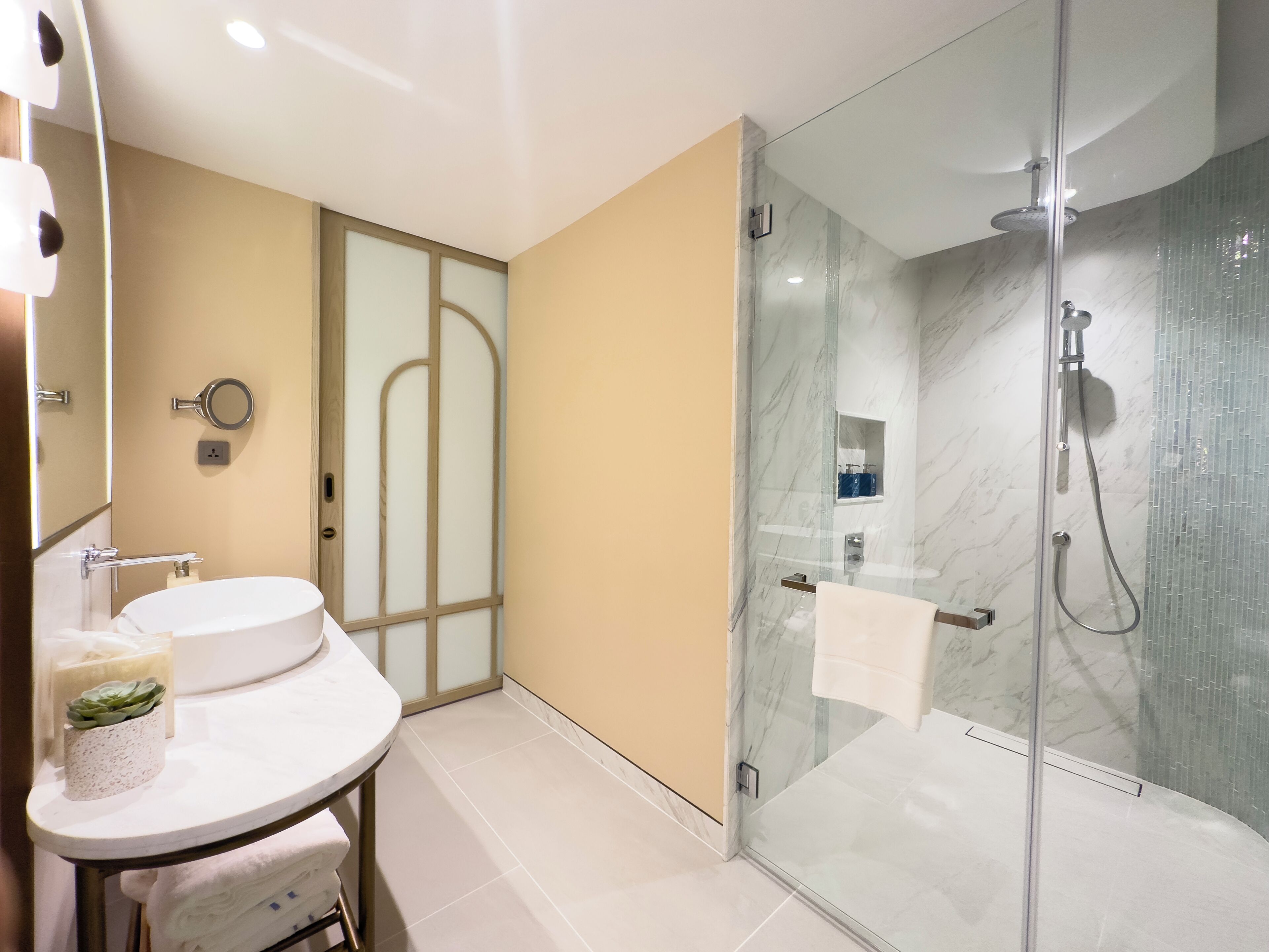A modern bathroom with a glass-enclosed shower, a round sink, and a vanity mirror.