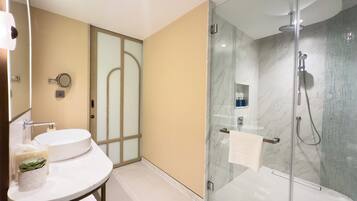 A modern bathroom with a glass-enclosed shower, a round sink, and a vanity mirror.