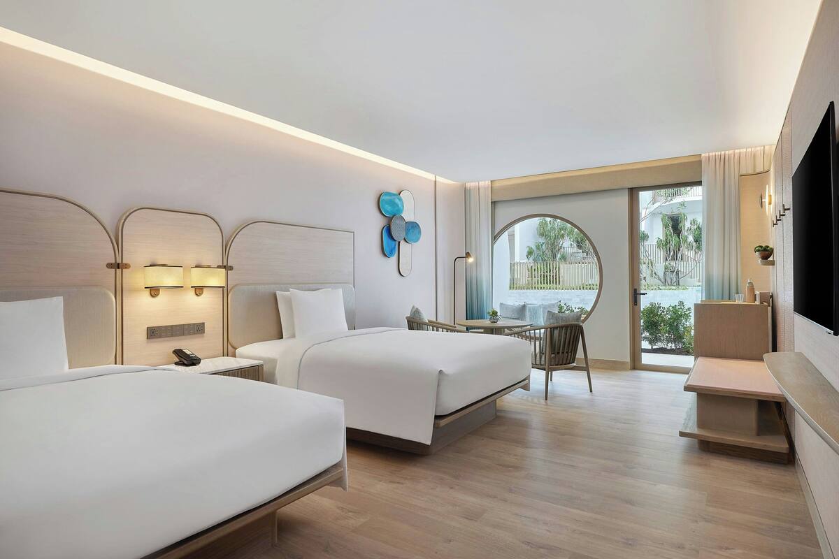 A hotel room with two beds, a desk, a chair, and a TV.