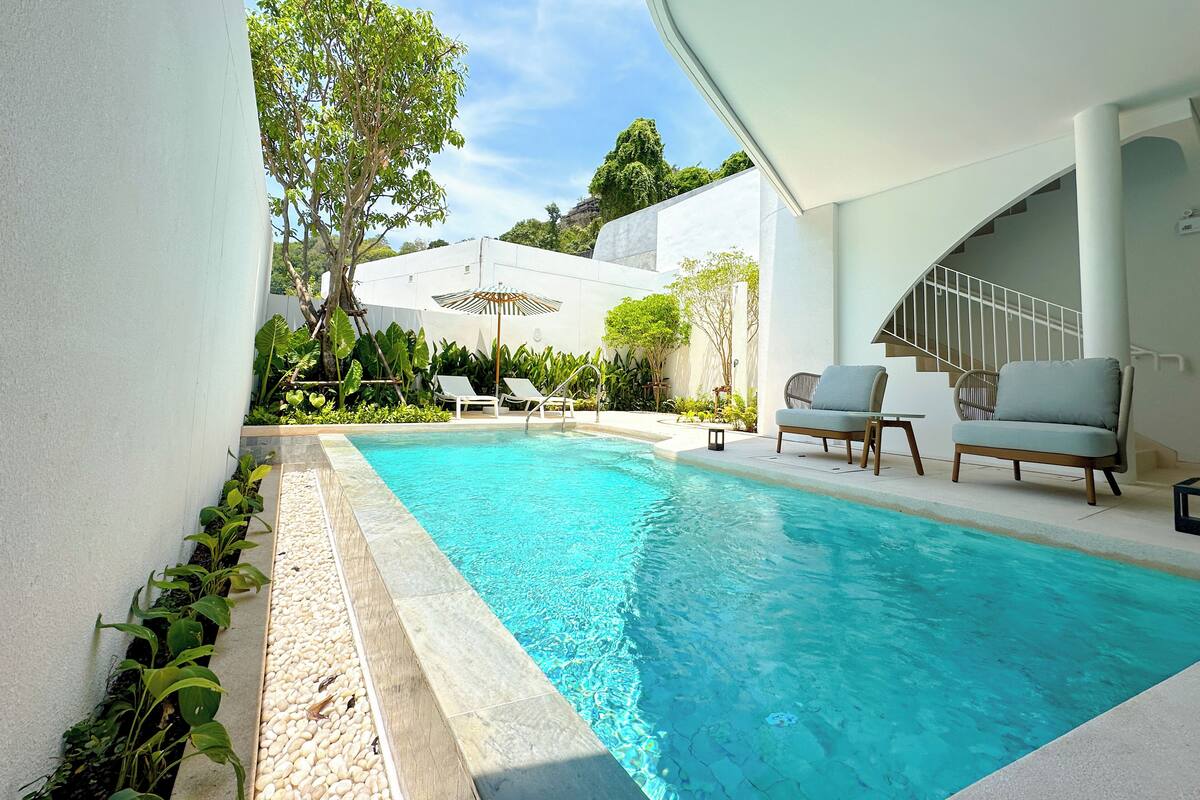 A modern pool area with a clear blue pool, lounge chairs, and a staircase leading to an upper level.