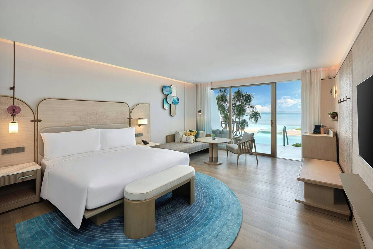 A modern hotel room with a large bed, a seating area, a TV, and a view of the ocean.