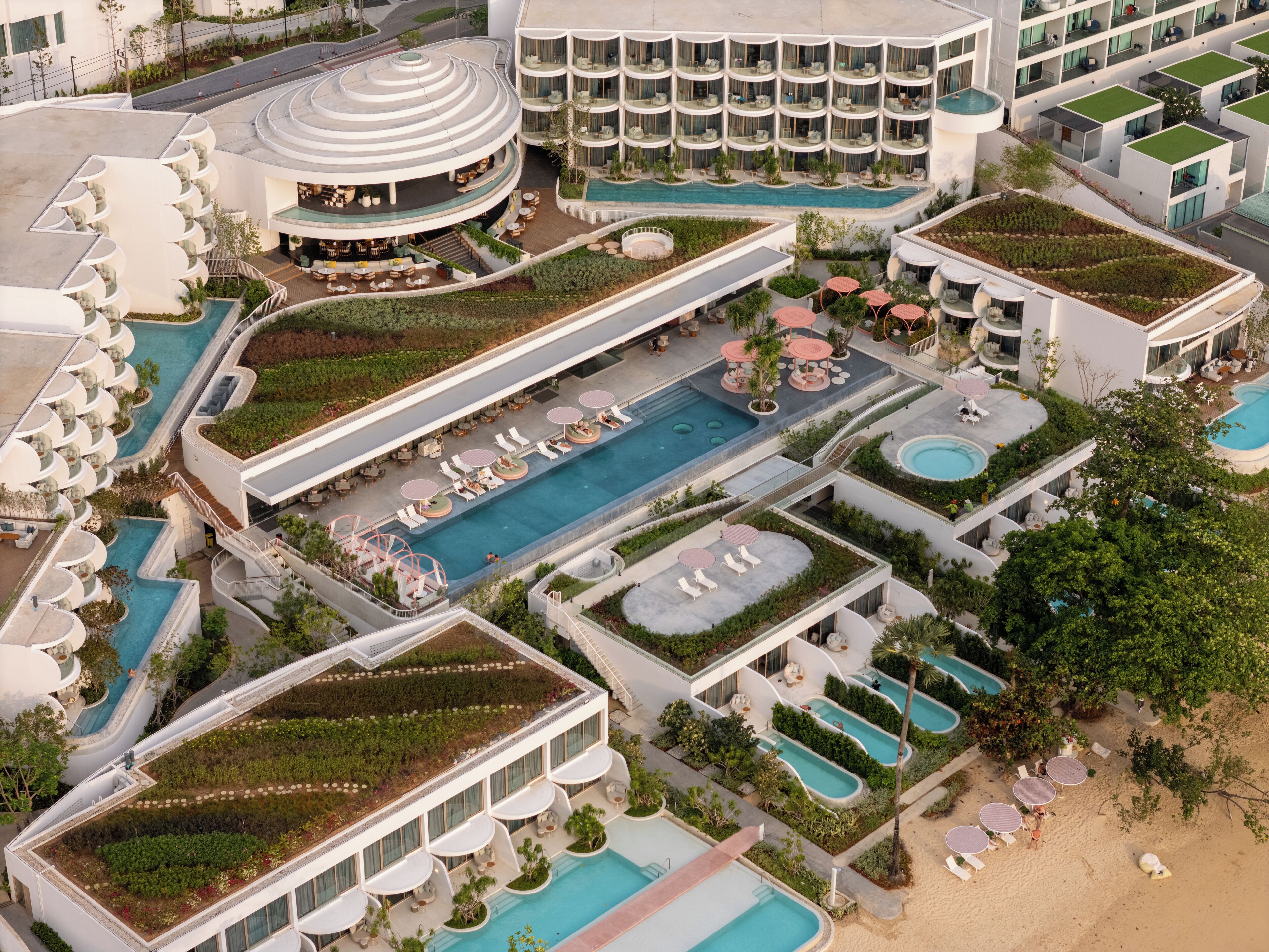 An aerial view of a hotel with multiple swimming pools, rooftop gardens, and outdoor seating areas.